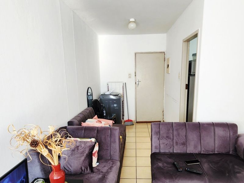 A compact living area featuring tiled flooring and neutral walls, providing a functional space with direct access to adjacent rooms.