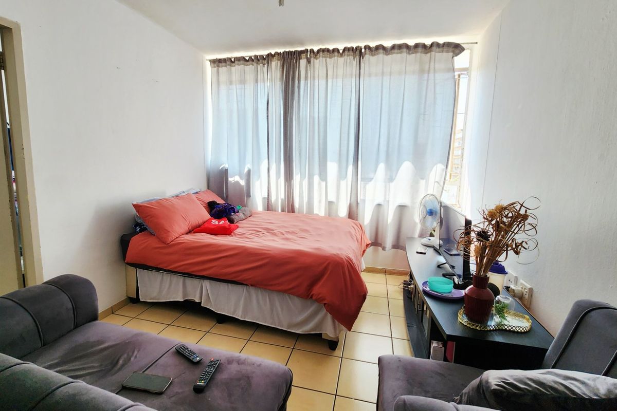 A compact bedroom featuring tiled flooring and a large window with curtain tracks, offering a functional space with potential for cosmetic updates.