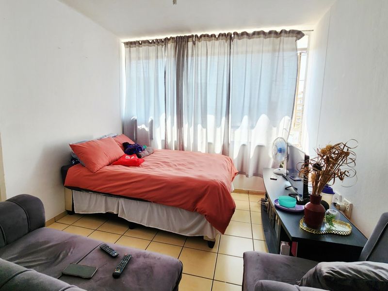 A compact bedroom featuring tiled flooring and a large window with curtain tracks, offering a functional space with potential for cosmetic updates.