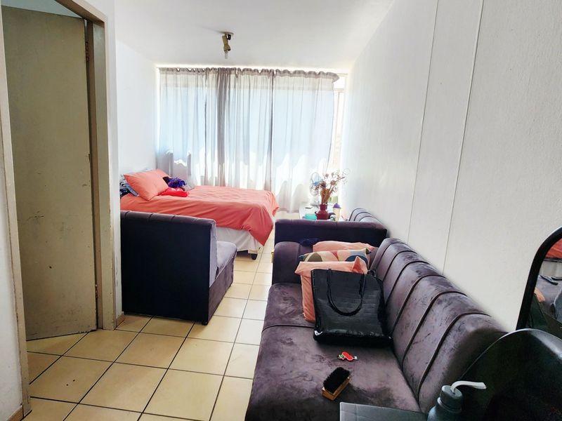 An open-plan living and sleeping area featuring ceramic floor tiles and access to a balcony through a sliding glass door.