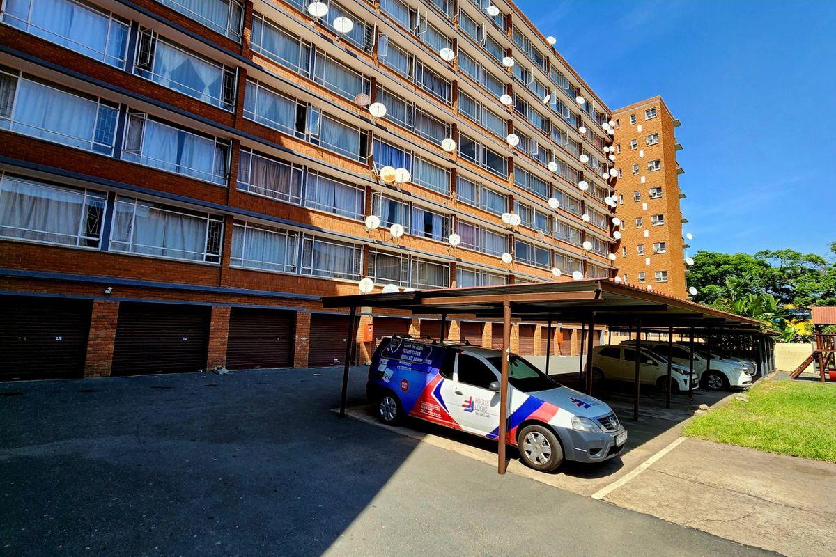 Exterior view of a multi-story brick apartment building featuring ground-level garages and a covered parking area.