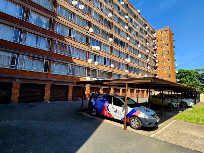 Exterior view of a multi-story brick apartment building featuring ground-level garages and a covered parking area.