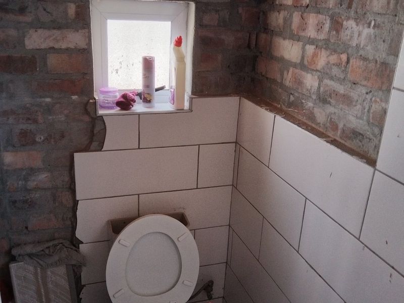 A bathroom in need of renovation, featuring a toilet, partially tiled walls, and exposed brickwork requiring finishing and plastering.