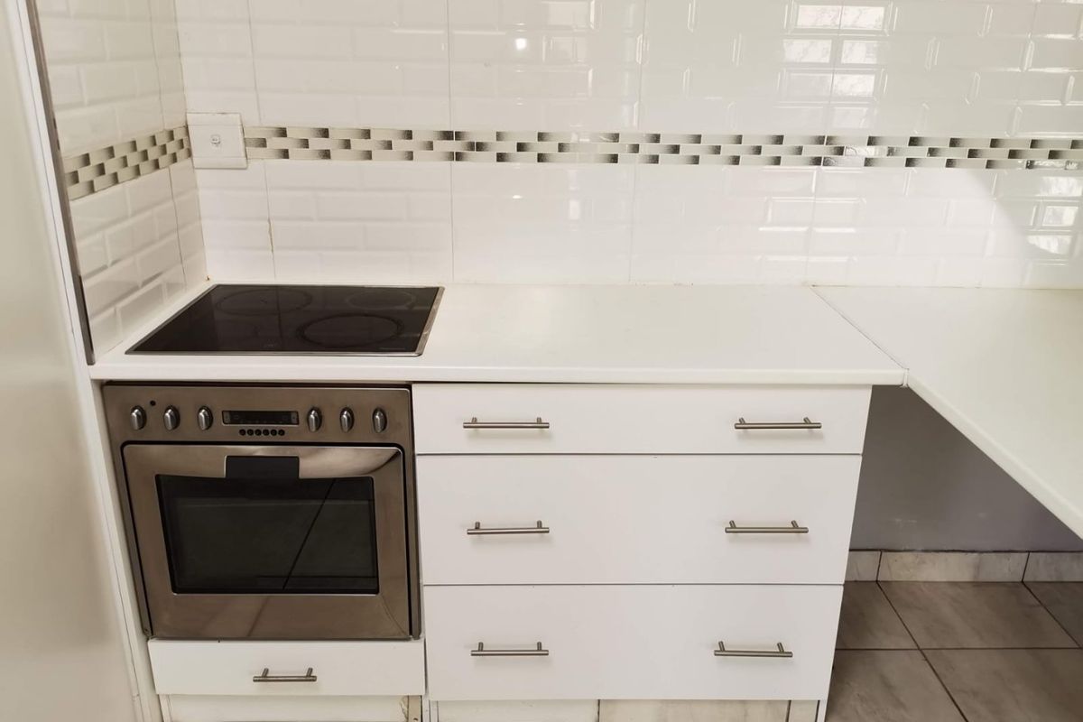 A clean, modern kitchen area featuring white cabinetry, a built-in oven, an electric hob, and a classic subway tile backsplash.