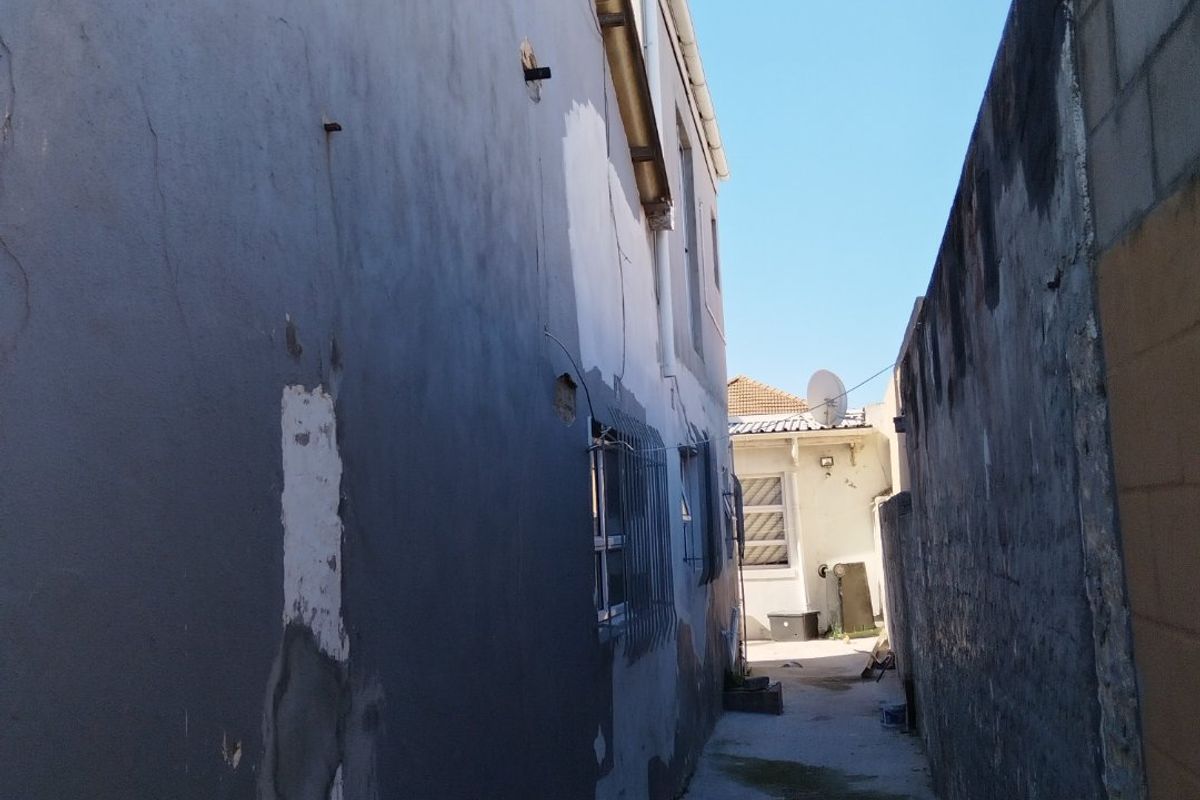 A narrow side passage between the house and a boundary wall, showing significant wear to the exterior plaster and paintwork.