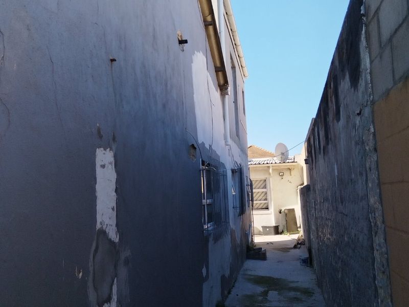 A narrow side passage between the house and a boundary wall, showing significant wear to the exterior plaster and paintwork.