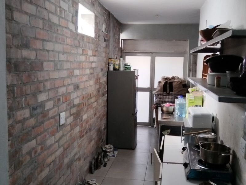 A narrow scullery or utility area featuring exposed brickwork, tiled floors, and functional metal shelving with built-in cabinetry for storage and food preparation.