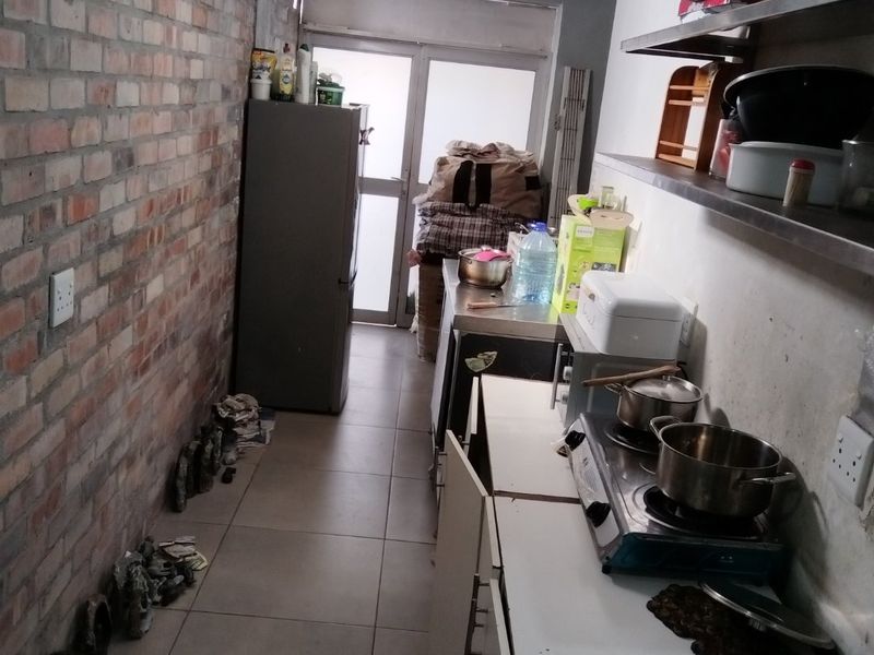 A functional scullery area featuring exposed brickwork, tiled flooring, and practical stainless steel shelving with built-in cabinetry for additional storage and prep space.