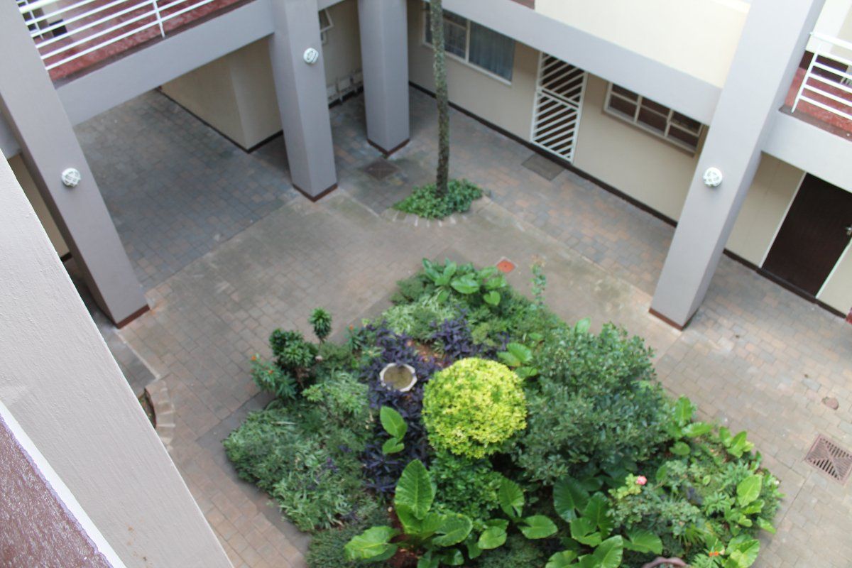 An elevated view of an apartment complex courtyard featuring paved flooring, structural columns, and a central landscaped garden area.