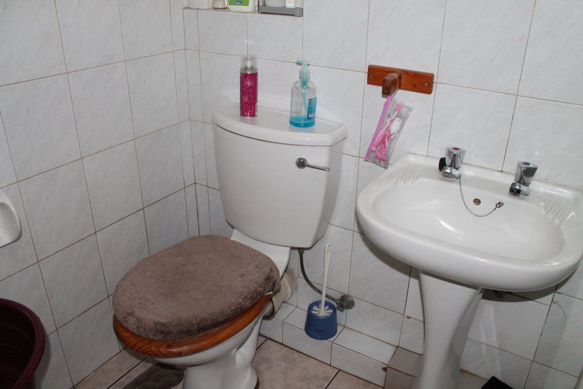 A compact bathroom featuring a standard pedestal basin and toilet with white ceramic wall tiling and tiled flooring.