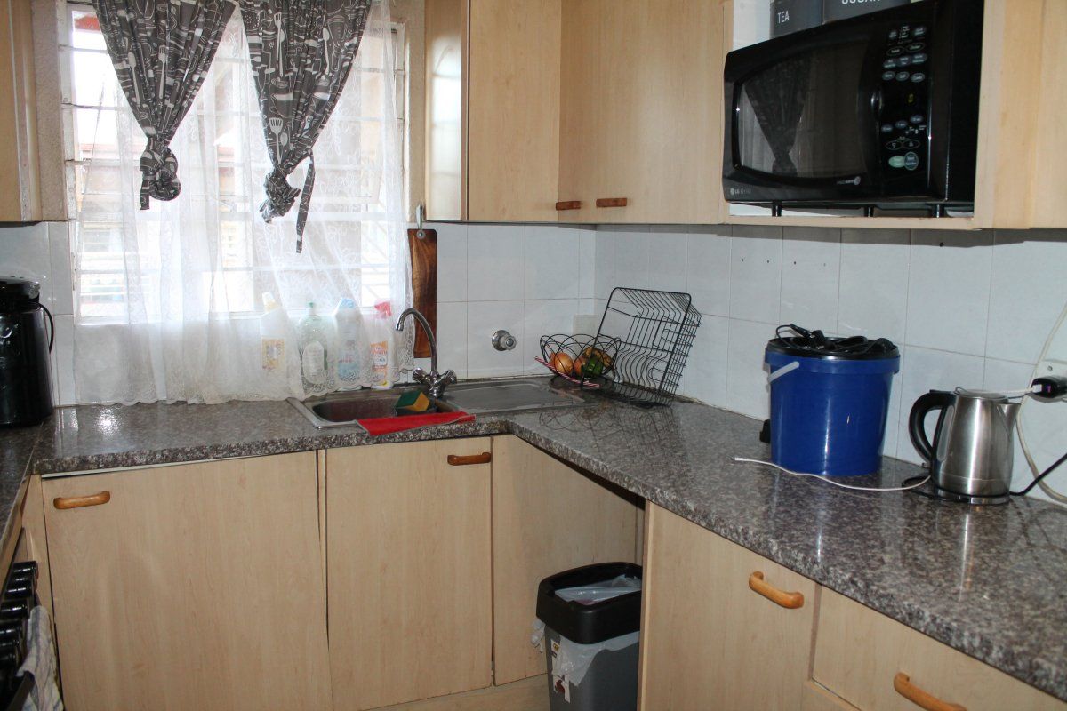 A functional kitchen featuring laminate cabinetry, granite-look countertops, a stainless steel sink, and a built-in microwave with tiled splashbacks.
