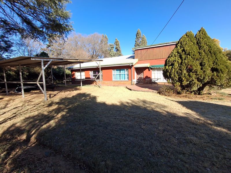 Rear view of the property featuring a carport, paved patio area, and established garden surroundings.
