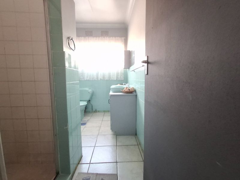 A dated bathroom featuring original pastel wall tiles, a vanity basin, toilet, and a separate shower enclosure.