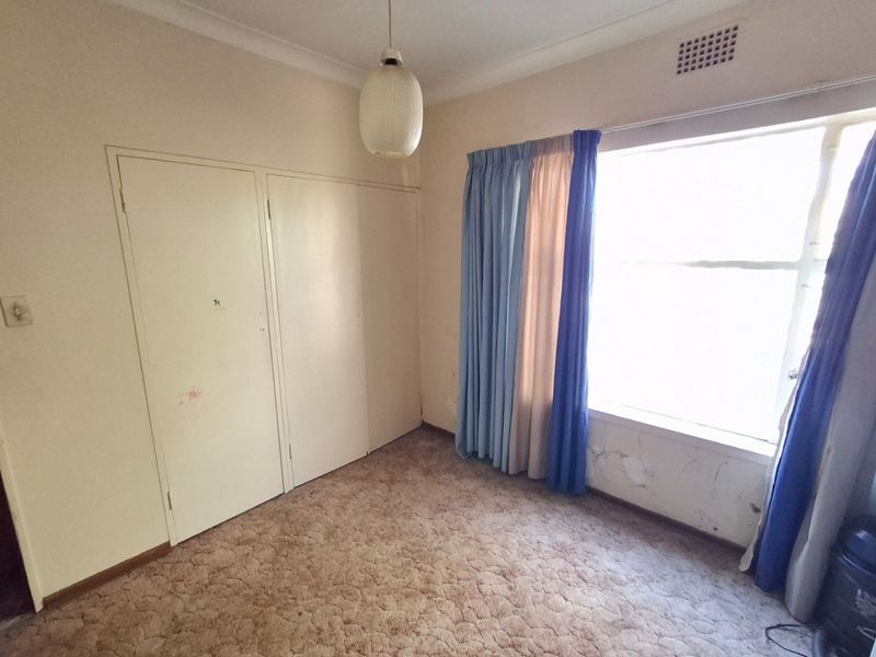 An empty bedroom featuring a built-in wardrobe, carpet flooring, and a large window. The room requires cosmetic updates to address wall surface damage.