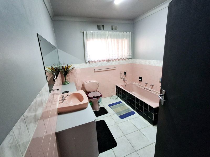 A dated bathroom featuring a pink bathtub, matching pink vanity basin, and toilet, with tiled flooring and wall splashbacks.