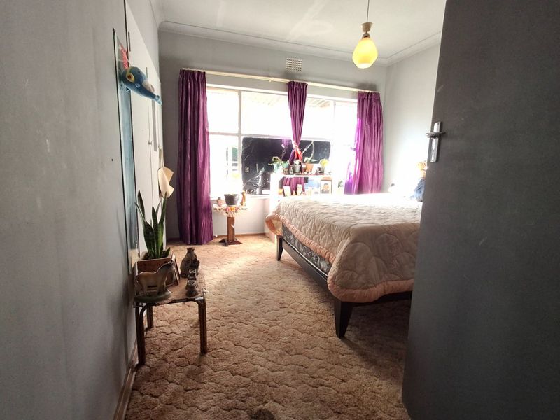 A bedroom featuring large windows for natural light, carpeted flooring, and a central ceiling light fixture, offering a functional space ready for updates.