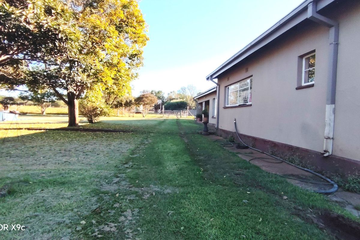 A view of the rear exterior of the farm property, featuring a lawn area, mature trees, and a concrete pathway along the building facade.