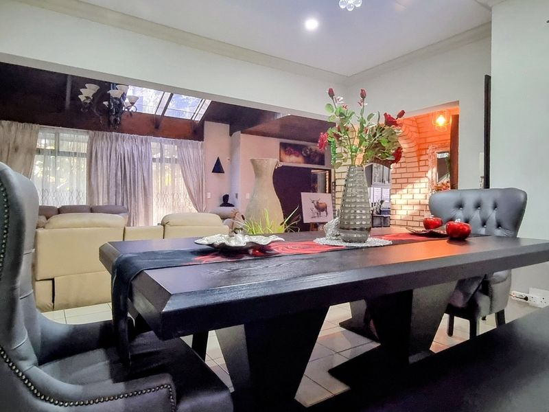 Spacious open-plan dining and living area featuring tiled floors, exposed timber beams, a skylight, and a warm brick feature wall.