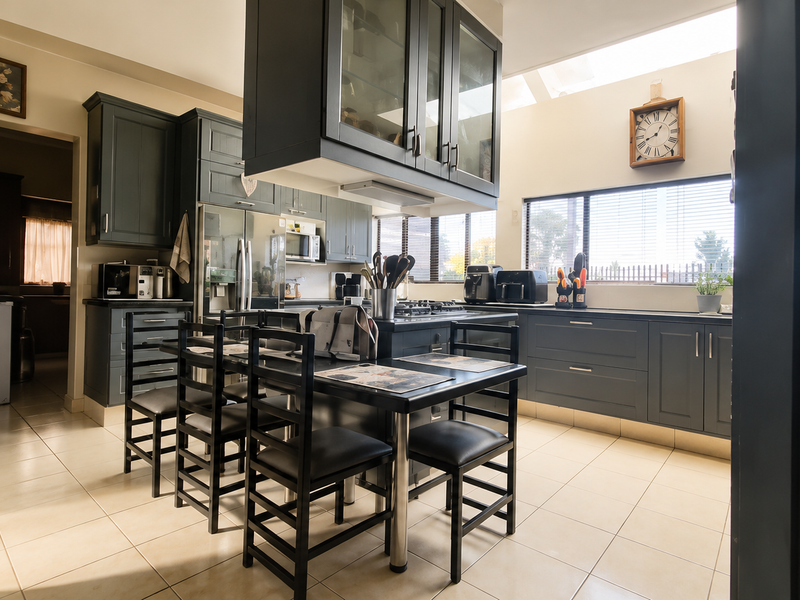 A well-appointed kitchen featuring dark cabinetry, a central island with a gas hob, tiled flooring, and a skylight providing ample natural light.