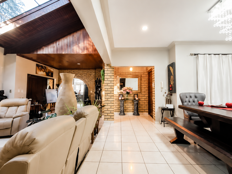 Spacious open-plan living and dining area featuring a high vaulted timber ceiling with skylights, exposed brick accents, and elegant tiled flooring.