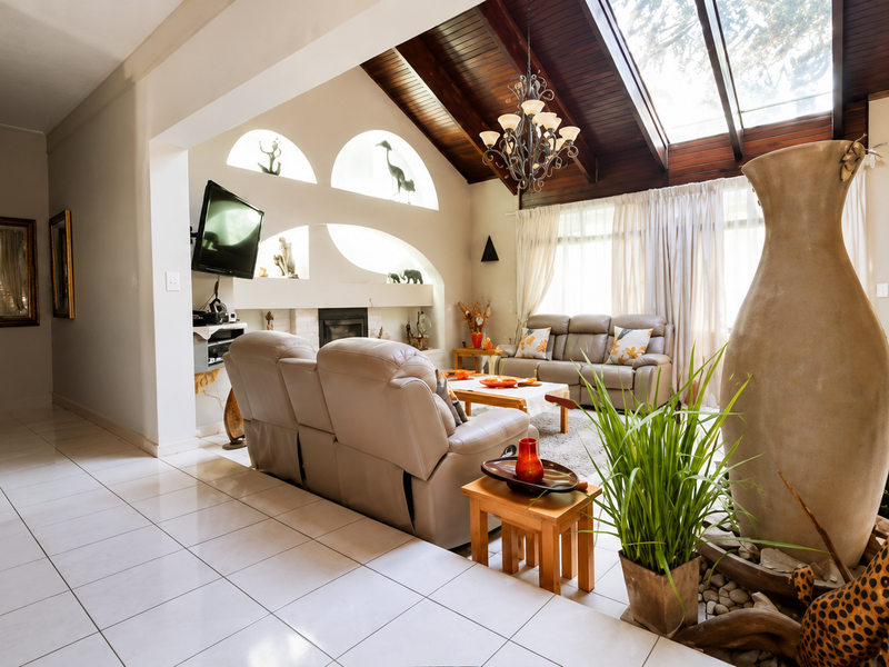Spacious living room featuring a dramatic vaulted timber ceiling with skylights, tiled flooring, and a built-in fireplace with decorative arched wall niches.
