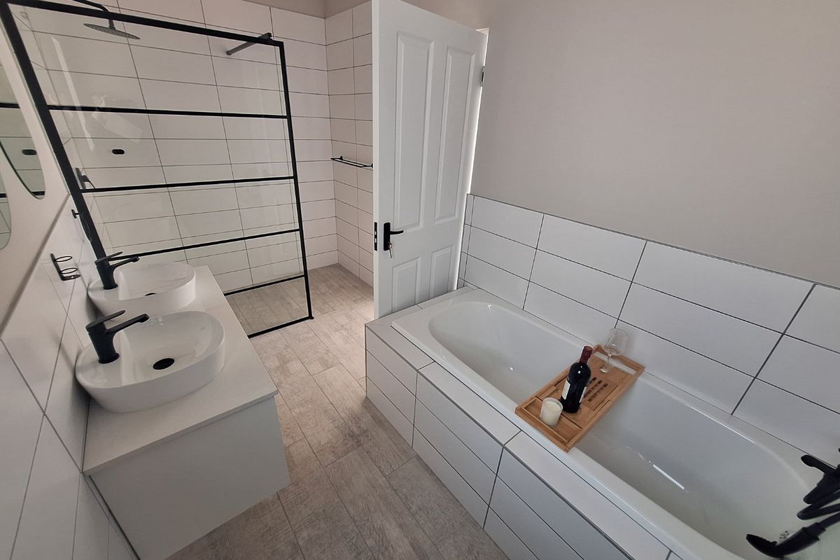 Modern bathroom featuring a double vanity with vessel sinks, a walk-in shower with black frame, and a built-in bathtub with white tiled surround.