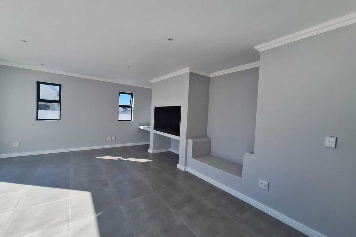 A bright, modern living room featuring large format floor tiles, a built-in fireplace, and a custom integrated bench seat with neutral grey finishes.