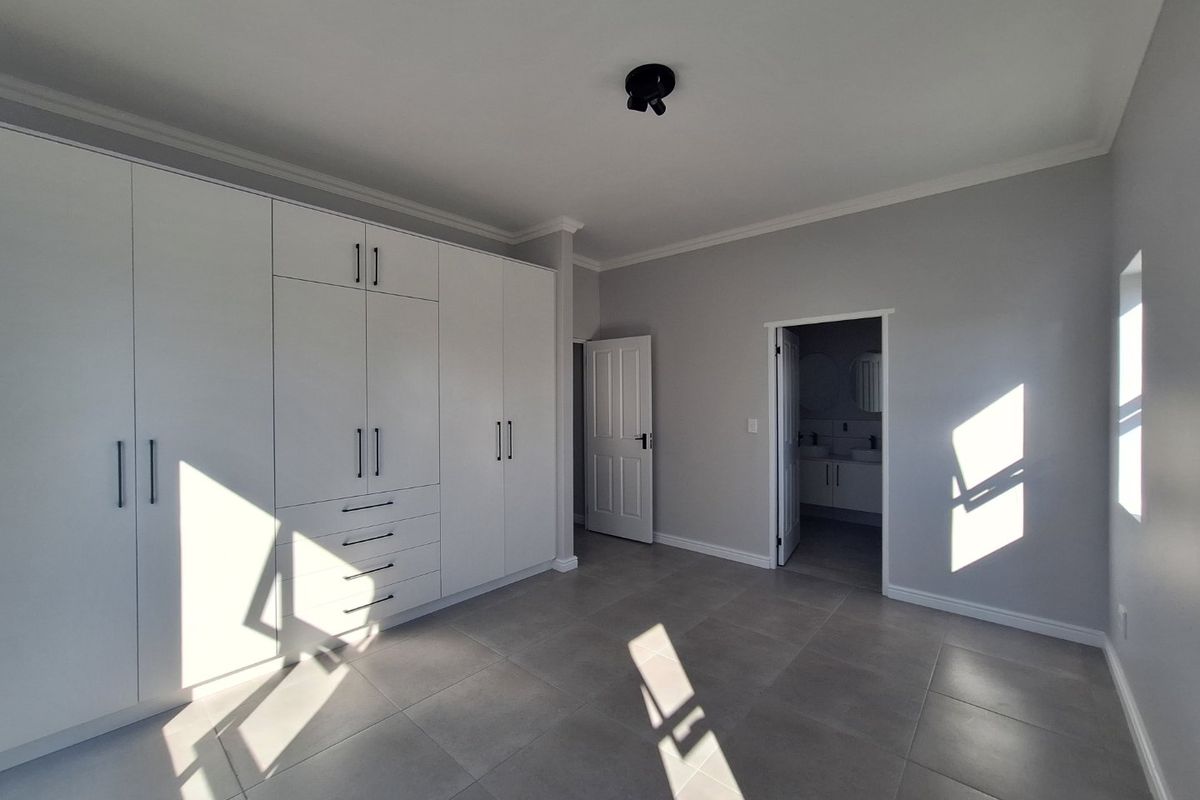 A bright, modern bedroom featuring built-in floor-to-ceiling cabinetry, neutral tiled flooring, and direct access to an en-suite bathroom.