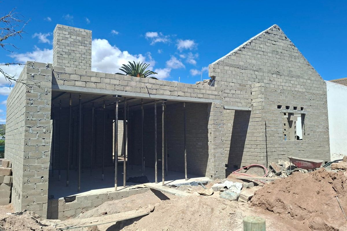 A rear view of a residential property currently under construction, featuring exposed concrete block walls, a chimney stack, and temporary steel support props.