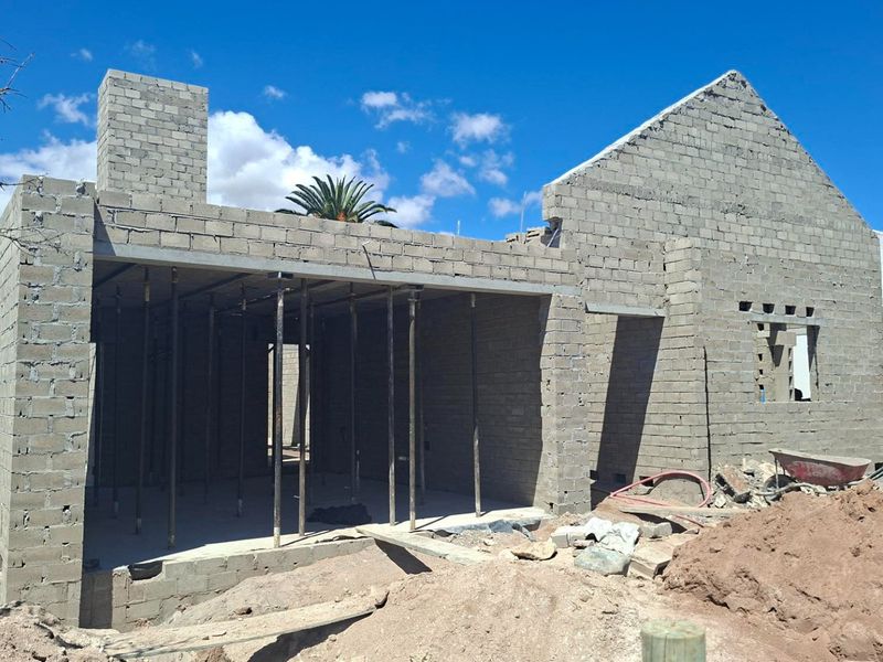 A rear view of a residential property currently under construction, featuring exposed concrete block walls, a chimney stack, and temporary steel support props.