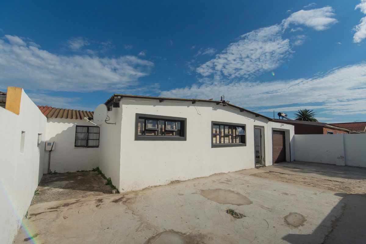 Rear exterior view of the property featuring a concrete driveway, garage access, and white painted walls with security features.