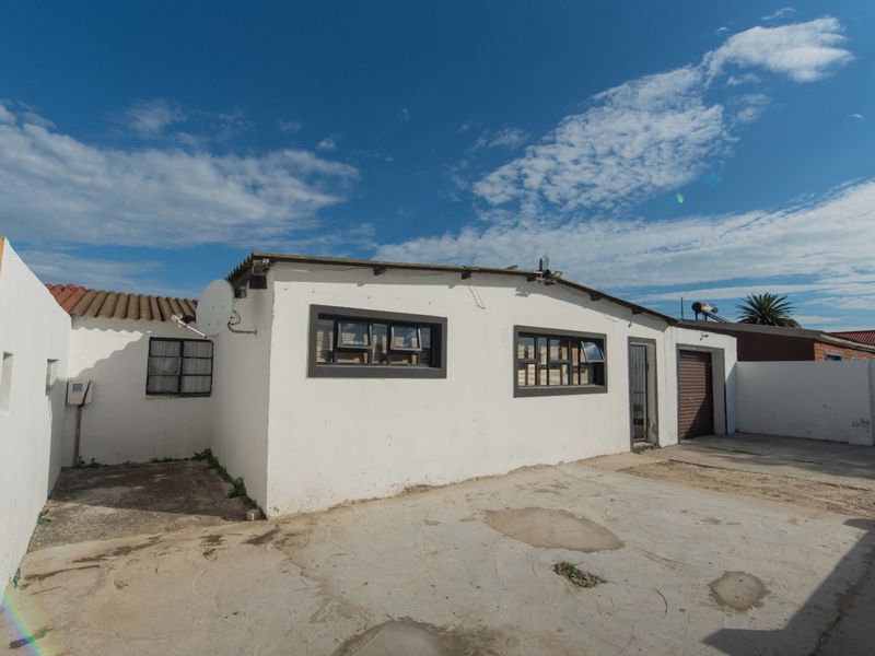 Rear exterior view of the property featuring a concrete driveway, garage access, and white painted walls with security features.