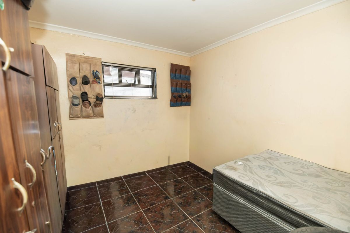 A bedroom featuring dark tiled flooring, a built-in wardrobe, and a window. The room requires cosmetic updates to the wall finishes.