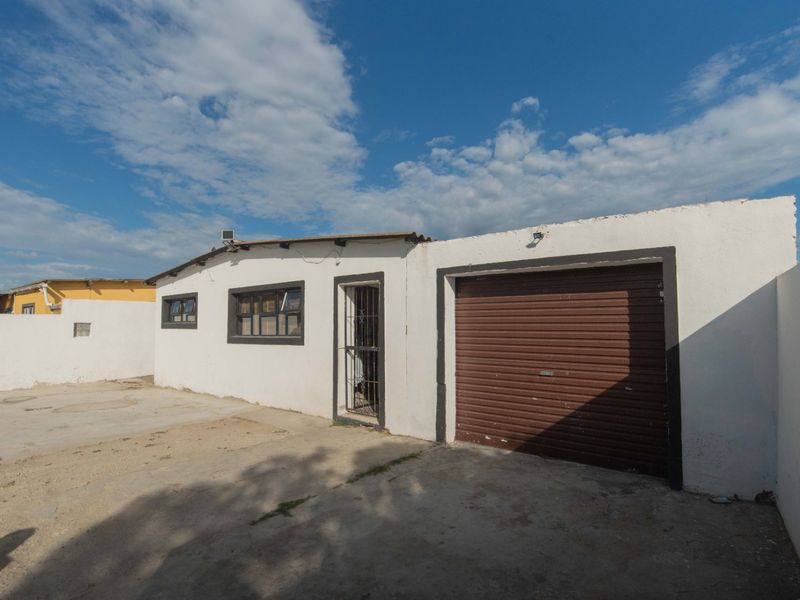 Front exterior view of a single-story house featuring a roller shutter garage door, security gate, and a concrete driveway.