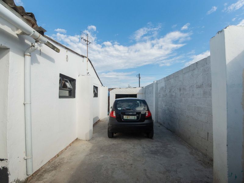 A narrow concrete driveway area between the house exterior and a cinder block boundary wall.