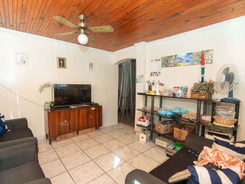 A living room featuring a timber tongue and groove ceiling, ceiling fan, and ceramic tiled flooring with an arched entryway.