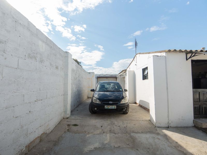 Exterior view of a driveway leading to a garage, featuring concrete paving and masonry boundary walls.