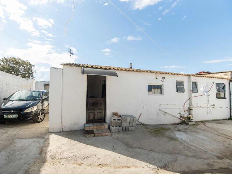 Rear exterior view of the property featuring a concrete paved yard, boundary walls, and visible external plumbing and electrical conduits.