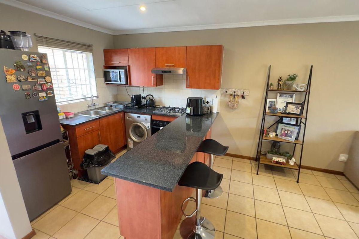 Compact kitchen featuring wood-veneer cabinetry, granite countertops, a breakfast bar, integrated gas hob, and built-in oven with extractor fan.