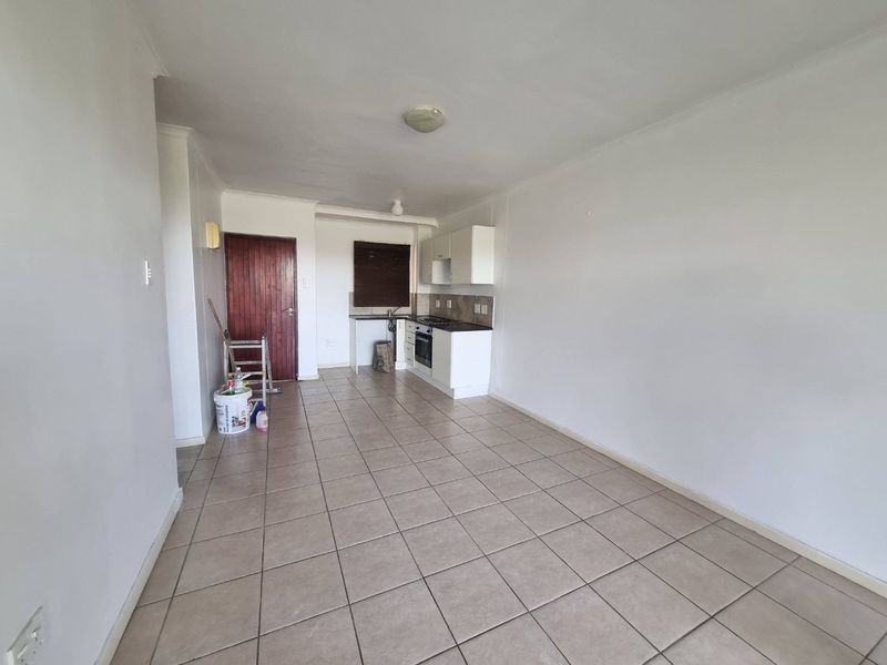 An open-plan living and kitchen area featuring tiled flooring, built-in cabinetry, and integrated cooking appliances in a neutral, vacant space.