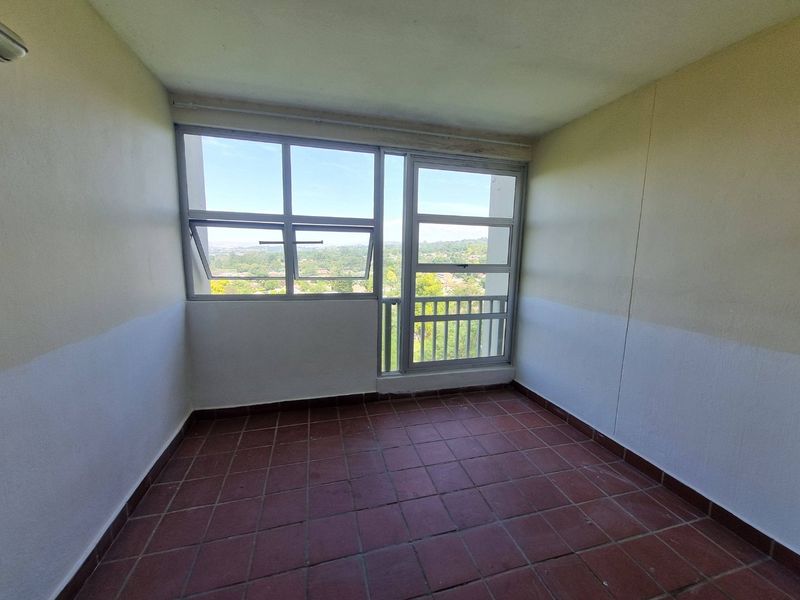An empty enclosed balcony featuring tiled flooring, large aluminium windows, and elevated views of the surrounding area.