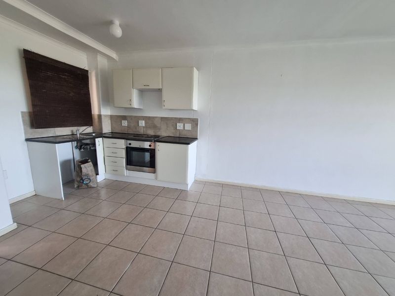 A compact, empty kitchen featuring tiled flooring, built-in cabinetry, an integrated oven and hob, and a tiled backsplash.