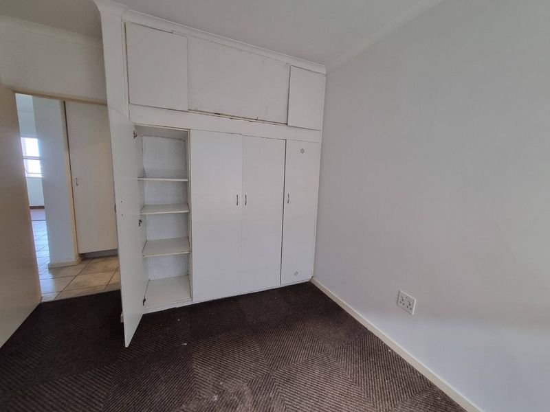 An empty bedroom featuring built-in cupboards with overhead storage and dark carpeting, offering a blank canvas for potential renovation or staging.