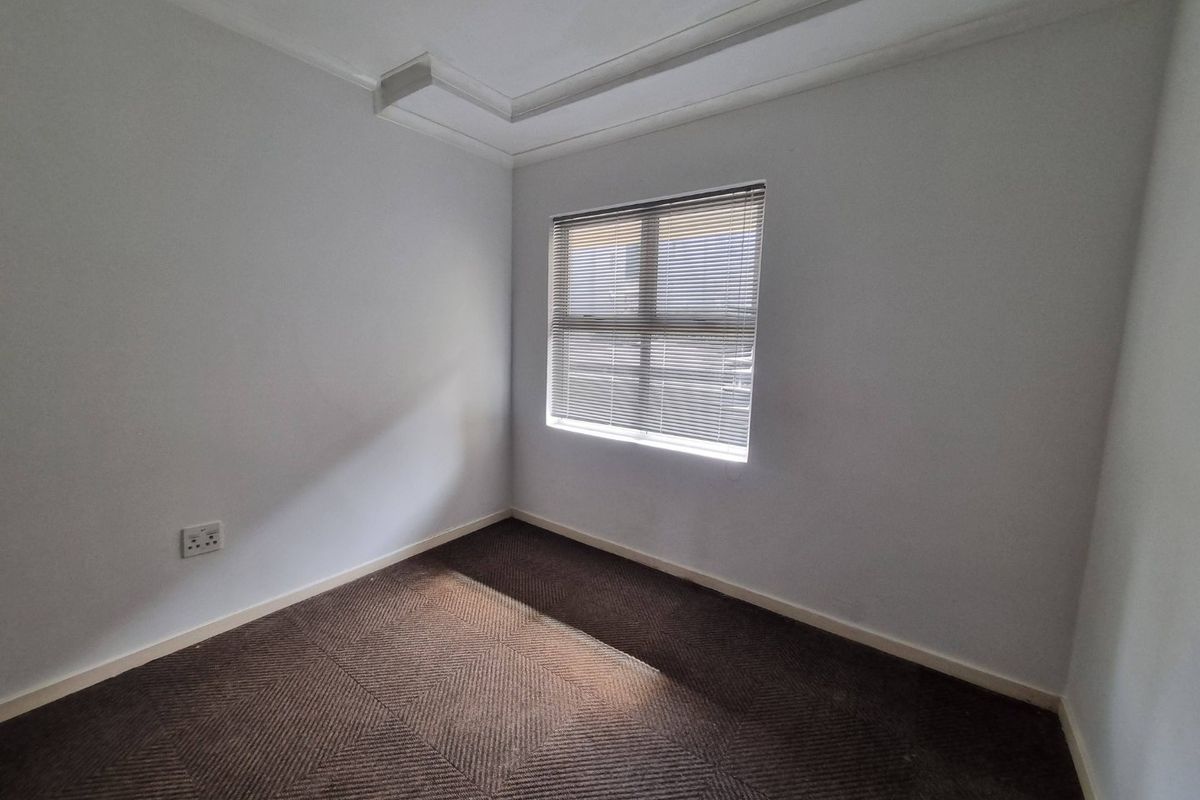 A clean, empty bedroom featuring neutral walls, carpeted flooring, and a window fitted with venetian blinds.