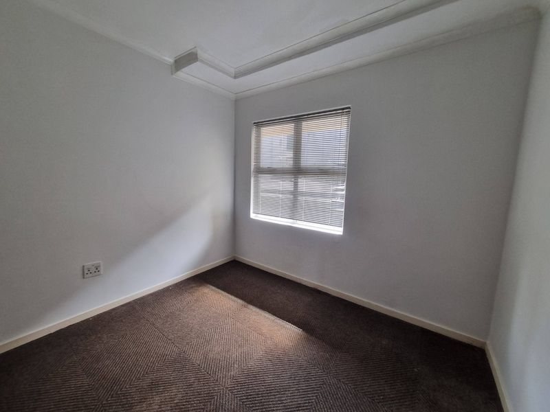 A clean, empty bedroom featuring neutral walls, carpeted flooring, and a window fitted with venetian blinds.