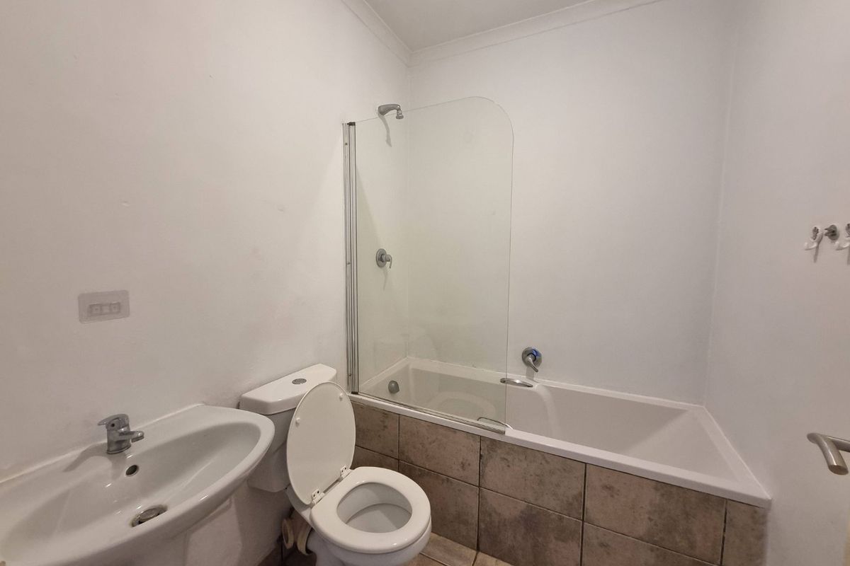 A functional bathroom featuring a pedestal basin, toilet, and a bathtub with a glass shower screen and tiled apron.