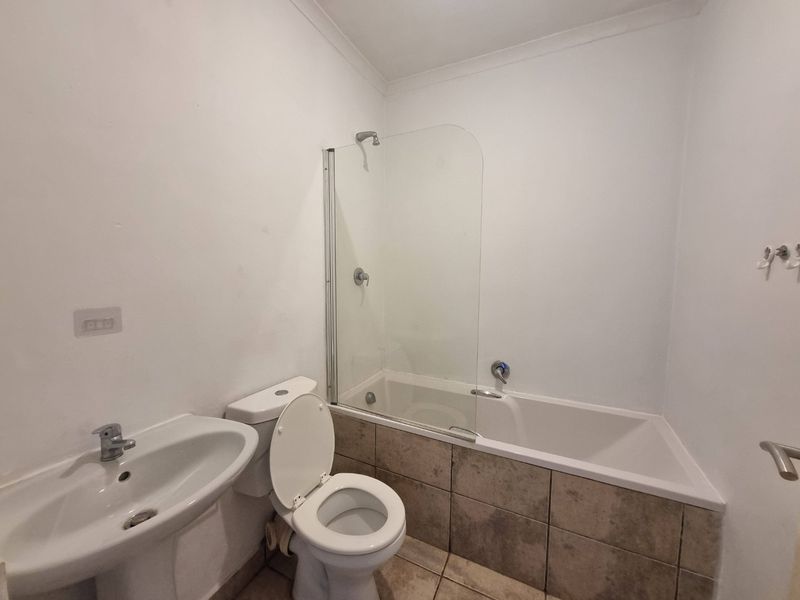 A functional bathroom featuring a pedestal basin, toilet, and a bathtub with a glass shower screen and tiled apron.