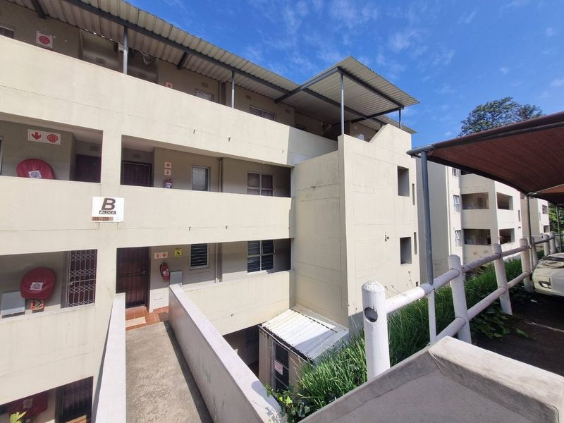 Exterior view of a multi-story apartment block featuring concrete walkways, security gates, and external fire safety equipment.