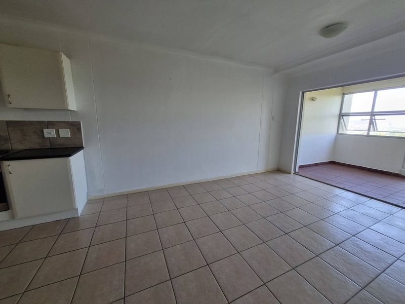 An open-plan living area featuring tiled flooring, compact kitchen cabinetry, and direct access to an attached balcony through a sliding door.