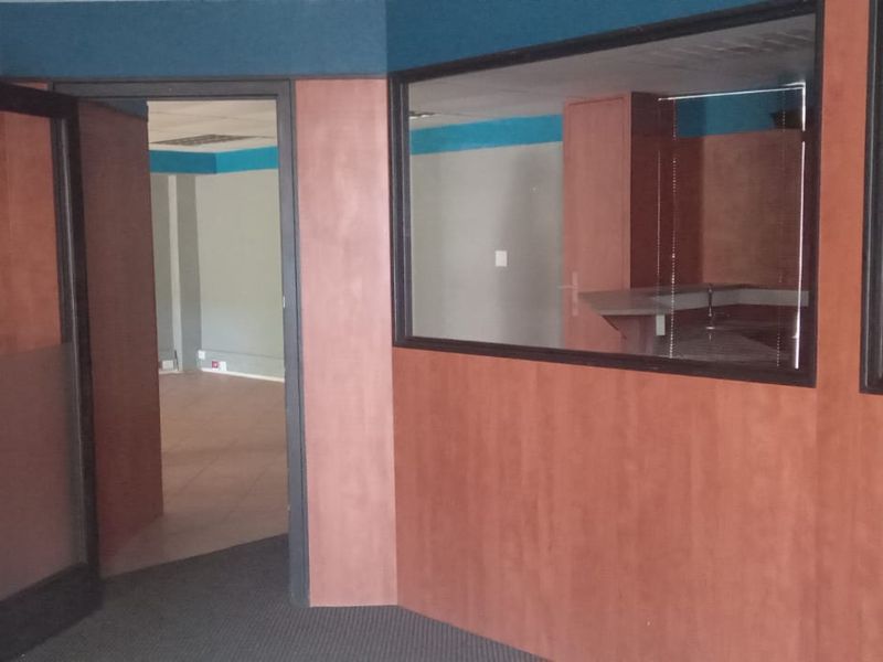 An empty commercial office space featuring wood veneer wall paneling, glass partitions, and carpeted flooring, suitable for a professional workspace layout.